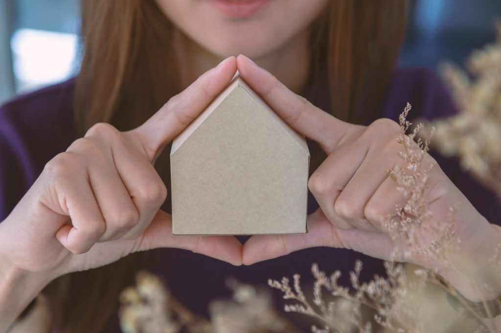 Woman holding paper house on her hands. Protect house- insurance concept.
